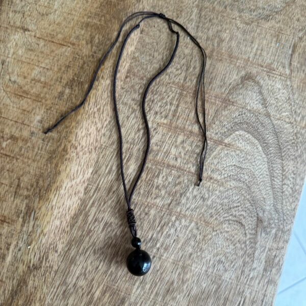 Pendentif Protection Ultime – Obsidienne Œil Céleste en sphère. Dimension de la pierre : 1.5 cm. Livré avec cordon en coton de couleur brun. Boutique de lithothérapie La Porte des Secrets